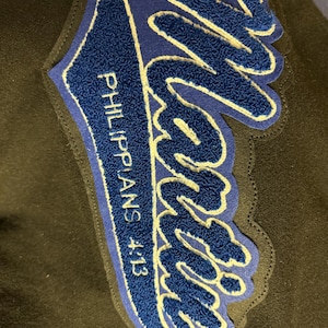 May include: Blue and white embroidered patch with the word "Martin" in a stylized font. The text "Philippians 4:13" is written below the word "Martin".