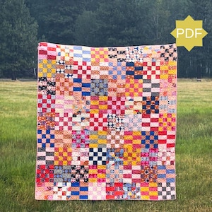 Puede incluir: Un edredón de patchwork colorido con un patrón de tablero de ajedrez, exhibido al aire libre. El edredón presenta cuadrados de telas rojas, amarillas, azules y negras. El fondo es un campo cubierto de hierba con árboles.