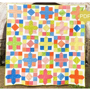 May include: A colorful quilt with a patchwork design. The quilt features squares and starburst patterns in shades of blue, orange, pink, green, and yellow. The quilt is displayed against a stone wall.