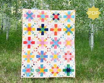 May include: A colorful quilt with a white background and a variety of geometric patterns in shades of pink, red, yellow, blue, and green. The quilt is hanging in a forest setting.
