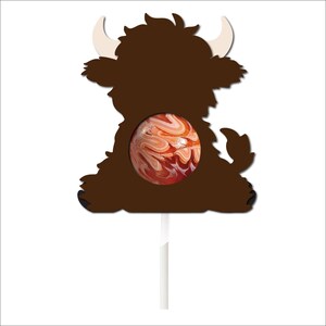 May include: A brown, cartoon-style, Highland cow lollipop mold with a swirl lollipop in the center. The mold is on a white stick.