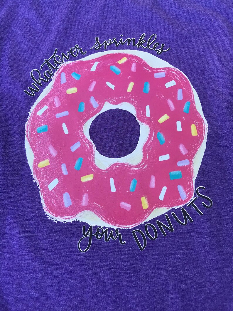 Purple graphic donut T-shirt with sprinkles designs on the donuts.
