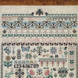 May include: A cross-stitch sampler with a white background and colorful embroidery. The sampler features a variety of floral motifs, a butterfly, a bee, a key, and a heart. The alphabet and numbers are also included in the design.