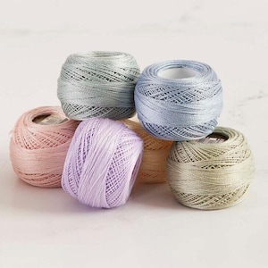 May include: A collection of six spools of colorful embroidery thread. The spools are in shades of pink, lavender, light blue, gray, beige, and light green. The thread is tightly wound, and the spools are arranged in a visually appealing manner.