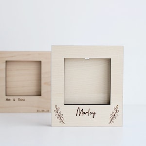 May include: Two wooden picture frames with a light brown finish. The frame on the left has the text "Me & You" and a date. The frame on the right has the text "Marley" with a leafy design.