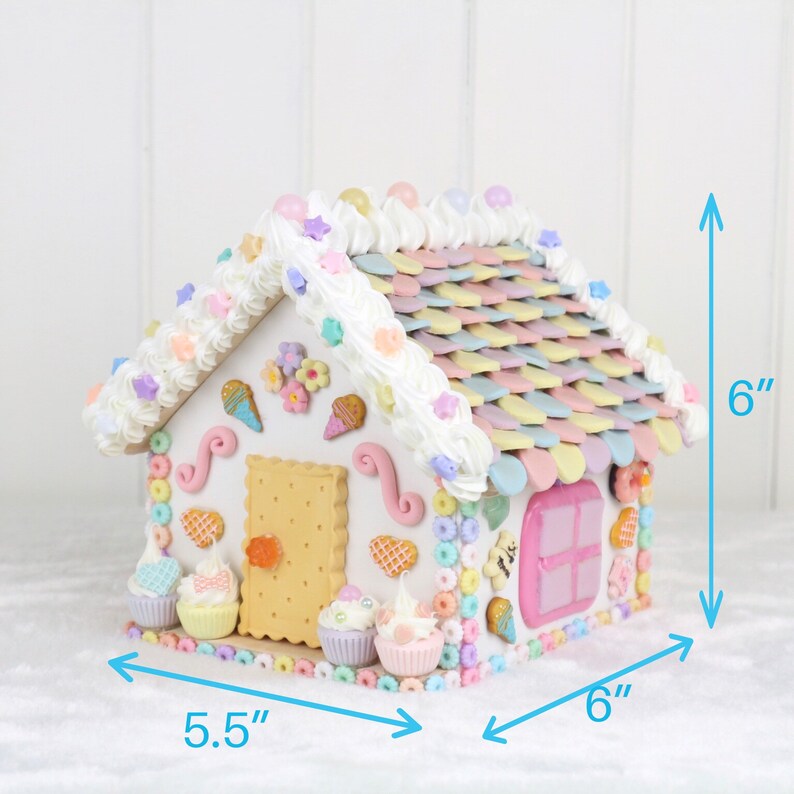 May include: A pastel-colored gingerbread house decorated with candy, frosting, and sprinkles. The house is 6 inches tall and 6 inches wide. The base of the house is 5.5 inches wide.