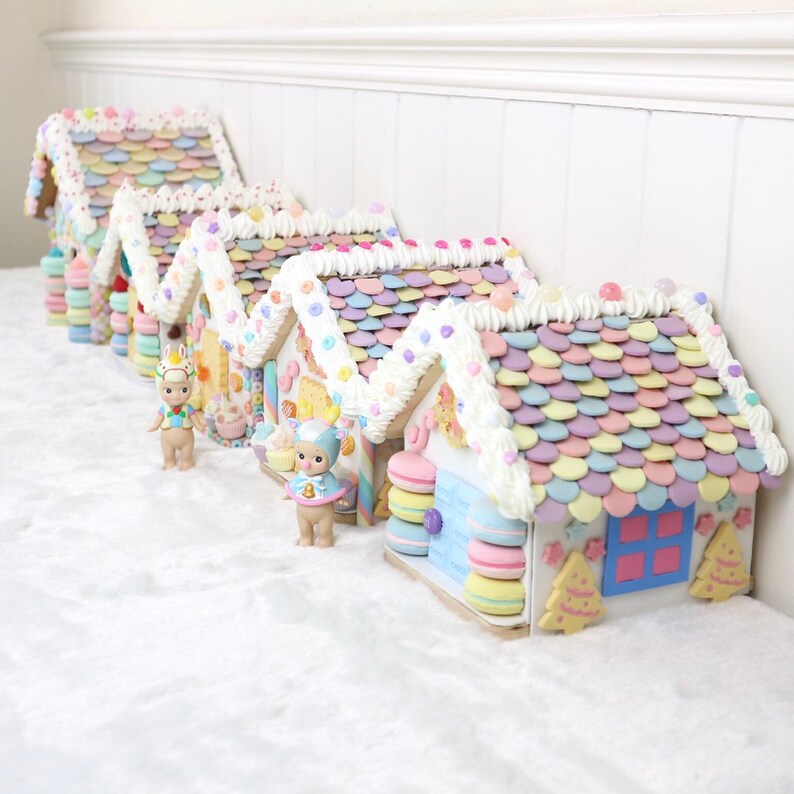 May include: A row of five pastel-colored gingerbread houses decorated with candy and frosting. Each house has a unique design and features a whimsical character figurine.