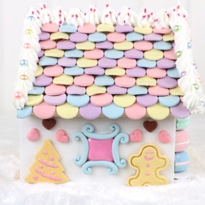 May include: A gingerbread house decorated with pastel-colored frosting and candy. The roof is covered in pastel-colored candy hearts. The house has a gingerbread tree, a gingerbread man, and a gingerbread window.