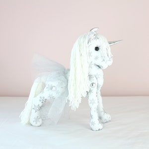 Großes Plüsch-Einhorn in weiß mit silberfarbener Borte. Geschenk für Blumenmädchen.