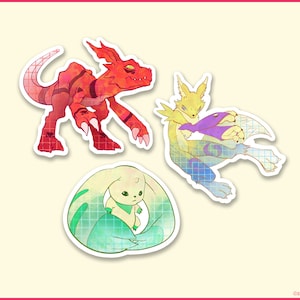 Peut inclure: Trois autocollants colorés représentant des monstres numériques de style dessin animé. Le premier autocollant est rouge et représente une créature rouge ressemblant à un dinosaure avec une griffe acérée. Le deuxième autocollant est jaune et représente une créature jaune ressemblant à un renard avec une queue violette. Le troisième autocollant est vert et représente une créature verte et blanche ressemblant à un lapin avec une longue queue.