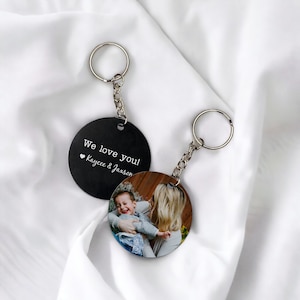 May include: Black round keychain with a photo of a woman holding a child. The text "We love you! Kaycee & Jaxson" is printed on the other side of the keychain.