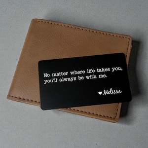 May include: A black metal card with the inscription "No matter where life takes you, you'll always be with me." and the name "Melissa" with a heart symbol. The card rests on a brown leather wallet.