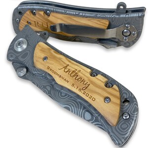 May include: A personalized pocket knife with a wood handle and a gray metal blade. The handle is engraved with the text "Anthony, Groomsman 5.16.2020".