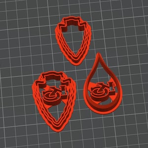 May include: Three red plastic cookie cutters shaped like a teardrop, a traditional arrowhead, and a modern arrowhead. Each cutter features a stylized "Z" inside.
