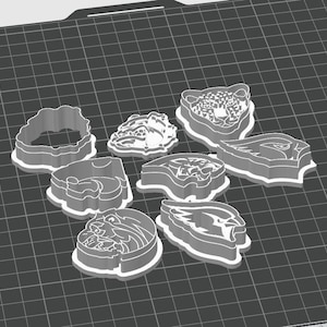 May include: A set of eight cookie cutters featuring various animal and sports team designs. The cutters are made of a white, textured plastic and are arranged on a black grid surface.