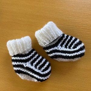 May include: A pair of black and white striped baby booties. The booties are knitted and have a white cuff.