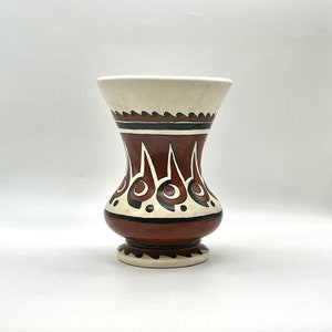 May include: A white ceramic vase with a brown and black geometric design. The vase has a wide mouth and a narrow base.