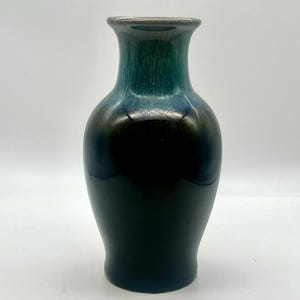 Puede incluir: Un jarrón pequeño de cerámica azul oscuro y verde con cuerpo redondeado y cuello estrecho.