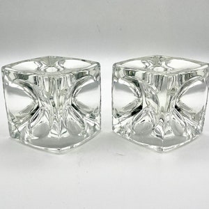 Puede incluir: Dos candelabros de vidrio transparente con un diseño geométrico. Los candelabros son de forma cuadrada con un centro hueco.