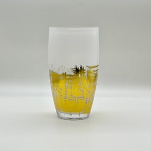May include: A frosted glass tumbler with a gold abstract design. The design is a series of lines and shapes that create a modern and stylish look.