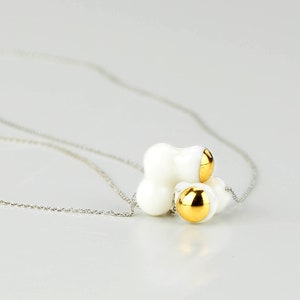 May include: A white ceramic necklace with a cluster of three round gold accents. The necklace is on a silver chain.