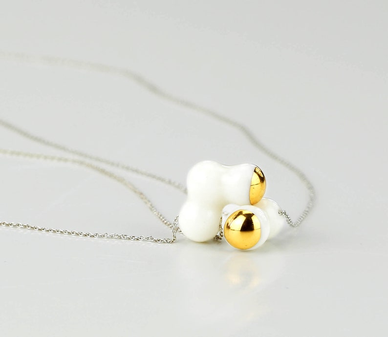 May include: A white ceramic necklace with a cluster of three round gold accents. The necklace is on a silver chain.