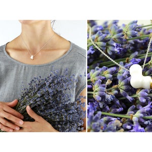 May include: A silver chain necklace with a white ceramic pendant shaped like a heart. The pendant has a gold accent on one side. The necklace is displayed on a bed of lavender flowers.