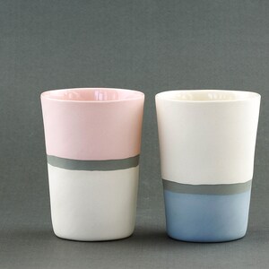 Pu&ograve; includere: Due tazze in ceramica con una striscia grigia e un colore diverso sulla met&agrave; inferiore di ogni tazza. Una tazza &egrave; rosa e bianca, l'altra &egrave; bianca e blu.