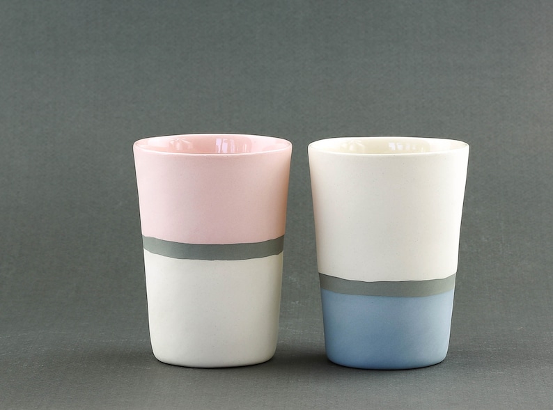 Pu&ograve; includere: Due tazze in ceramica con una striscia grigia e un colore diverso sulla met&agrave; inferiore di ogni tazza. Una tazza &egrave; rosa e bianca, l'altra &egrave; bianca e blu.