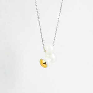 May include: A silver chain necklace with a white ceramic pendant. The pendant is shaped like a cluster of rounded forms with a gold accent on one side.
