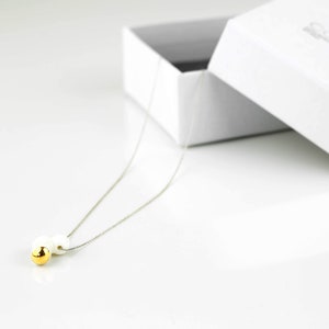 May include: A delicate silver chain necklace with a small gold bead and a white pearl bead pendant.