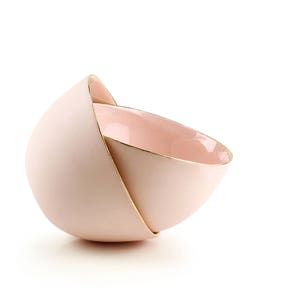 May include: Two pink ceramic bowls nested together. The top bowl has a gold rim.