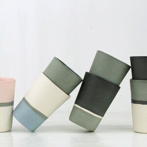 Pu&ograve; includere: Cinque tazze in ceramica con diverse combinazioni di colori. Le tazze sono impilate e si appoggiano l'una all'altra. I colori includono rosa, bianco, grigio, blu e nero.