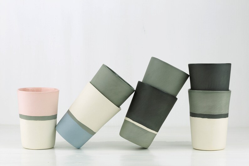 Pu&ograve; includere: Cinque tazze in ceramica con diverse combinazioni di colori. Le tazze sono impilate e si appoggiano l'una all'altra. I colori includono rosa, bianco, grigio, blu e nero.
