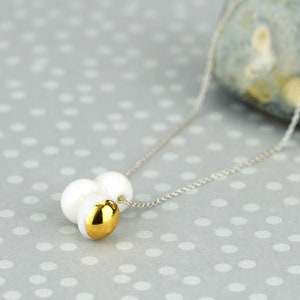 May include: A silver chain necklace with a pendant made of three white pearls and a gold accent.