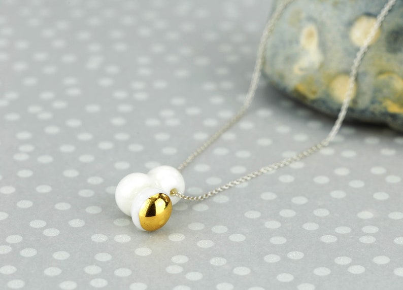 May include: A silver chain necklace with a pendant made of three white pearls and a gold accent.