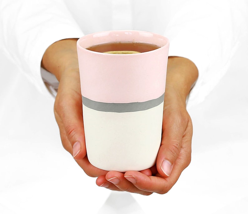 Pu&ograve; includere: Una tazza in ceramica rosa e bianca con una striscia grigia intorno al centro. La tazza &egrave; piena di un liquido marrone chiaro.