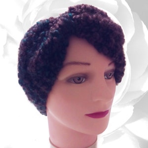 May include: A brown and teal crocheted headband with a twisted design. The headband is worn on a mannequin head.