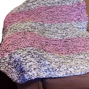 May include: A soft, chunky knit throw blanket with stripes of white, pink, and gray. The blanket is draped over a brown couch.