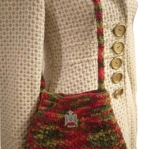 Puede incluir: Un bolso de mano de crochet en color rojo, verde y naranja. El bolso tiene un peque&ntilde;o amuleto plateado.