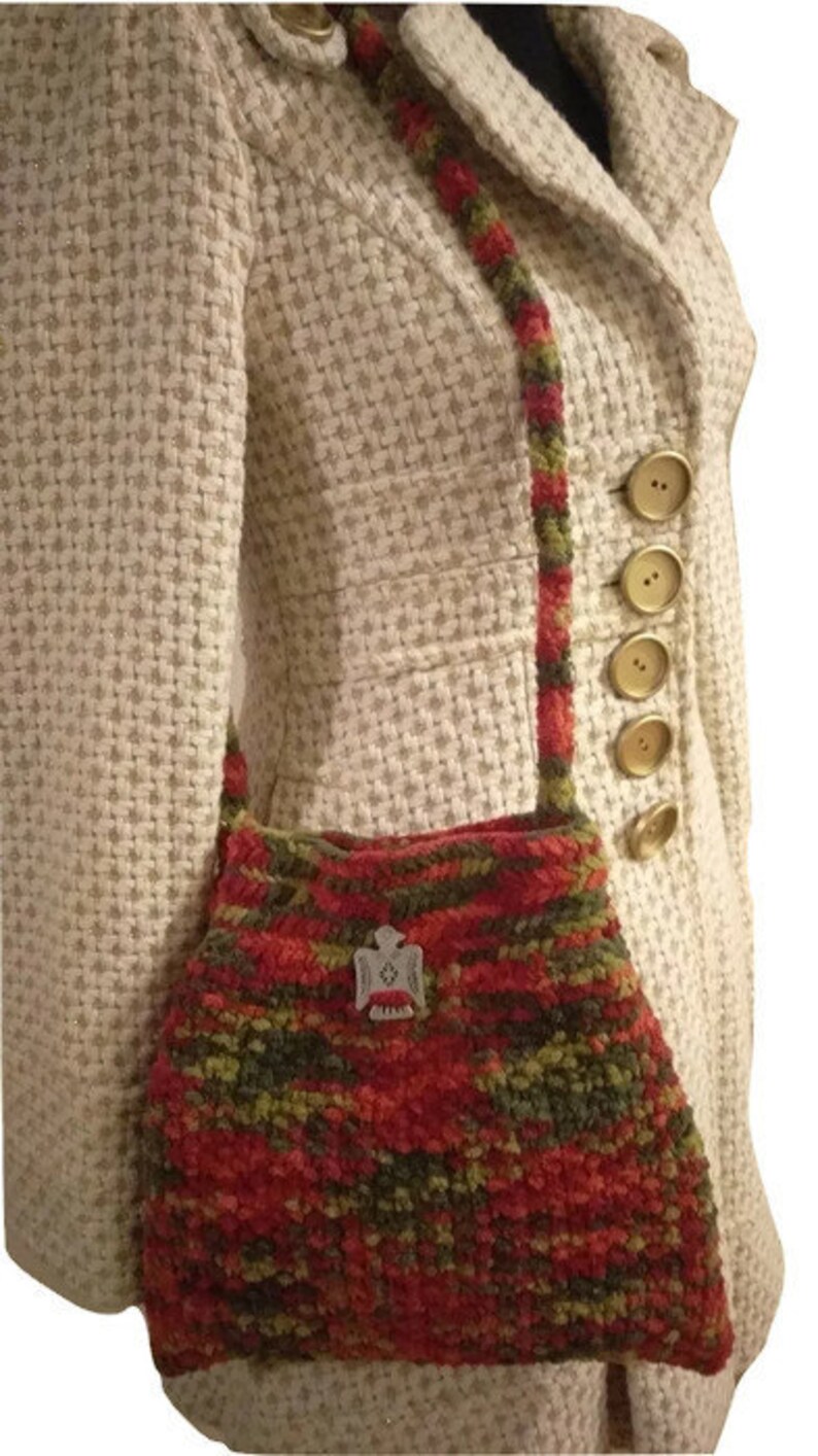 Puede incluir: Un bolso de mano de crochet en color rojo, verde y naranja. El bolso tiene un peque&ntilde;o amuleto plateado.