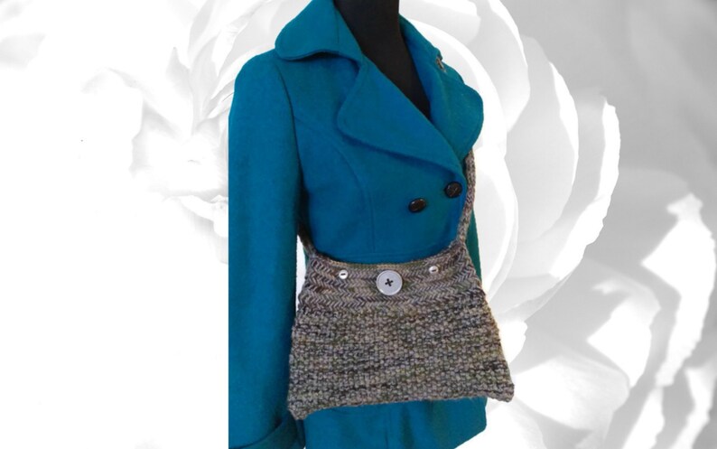May include: A teal blue peacoat with a knitted gray and brown crossbody bag. The bag has a large button on the front.