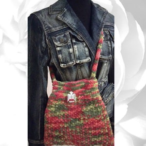 Puede incluir: Un bolso de mano de crochet en tonos verdes, rojos y rosas. El bolso tiene una correa larga y un dije de &aacute;guila plateado.
