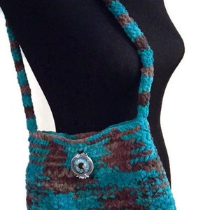 May include: A teal and brown crocheted shoulder bag with a decorative metal button. The bag has a long strap and is made of a soft, fuzzy yarn.