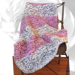 May include: A soft, striped throw blanket in shades of pink, white, and gray. The blanket is draped over a chair.