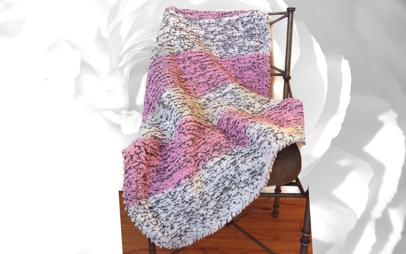 May include: A soft, striped throw blanket in shades of pink, white, and gray. The blanket is draped over a chair.