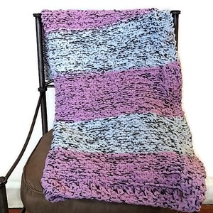 May include: A striped knitted throw blanket in shades of pink, gray, and white, draped over a brown chair.