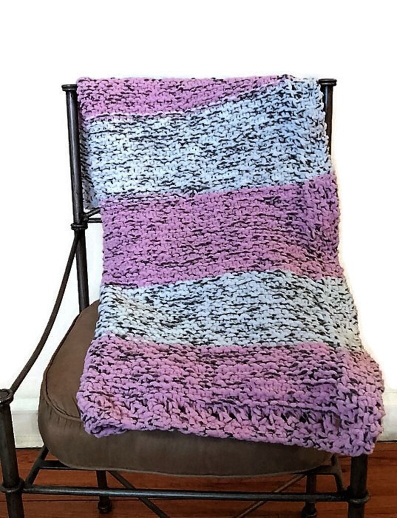 May include: A striped knitted throw blanket in shades of pink, gray, and white, draped over a brown chair.