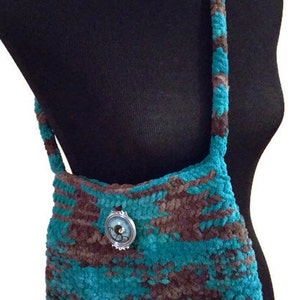 May include: A teal and brown crocheted shoulder bag with a silver and blue button accent.