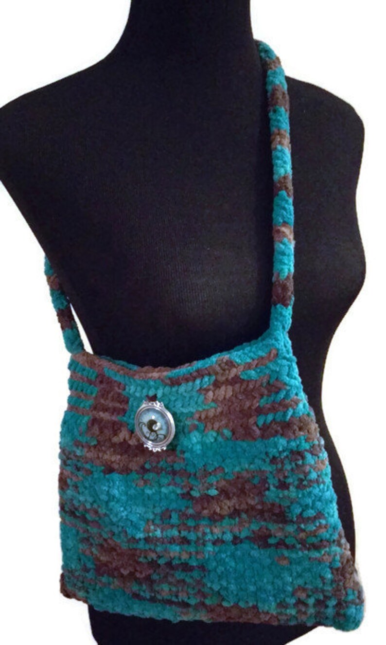 May include: A teal and brown crocheted shoulder bag with a silver and blue button accent.